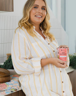 A woman with blonde hair is smiling and holds a tin of beef bone broth miso ramen