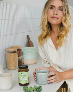 a woman holds on to a mug of broth made with beef bone broth native herbs