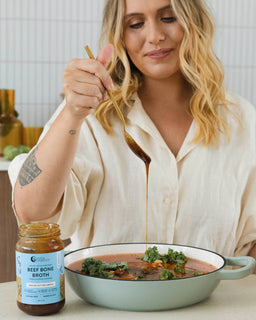 A woman adds a teaspoon of bone broth concentrate to a savoury dish